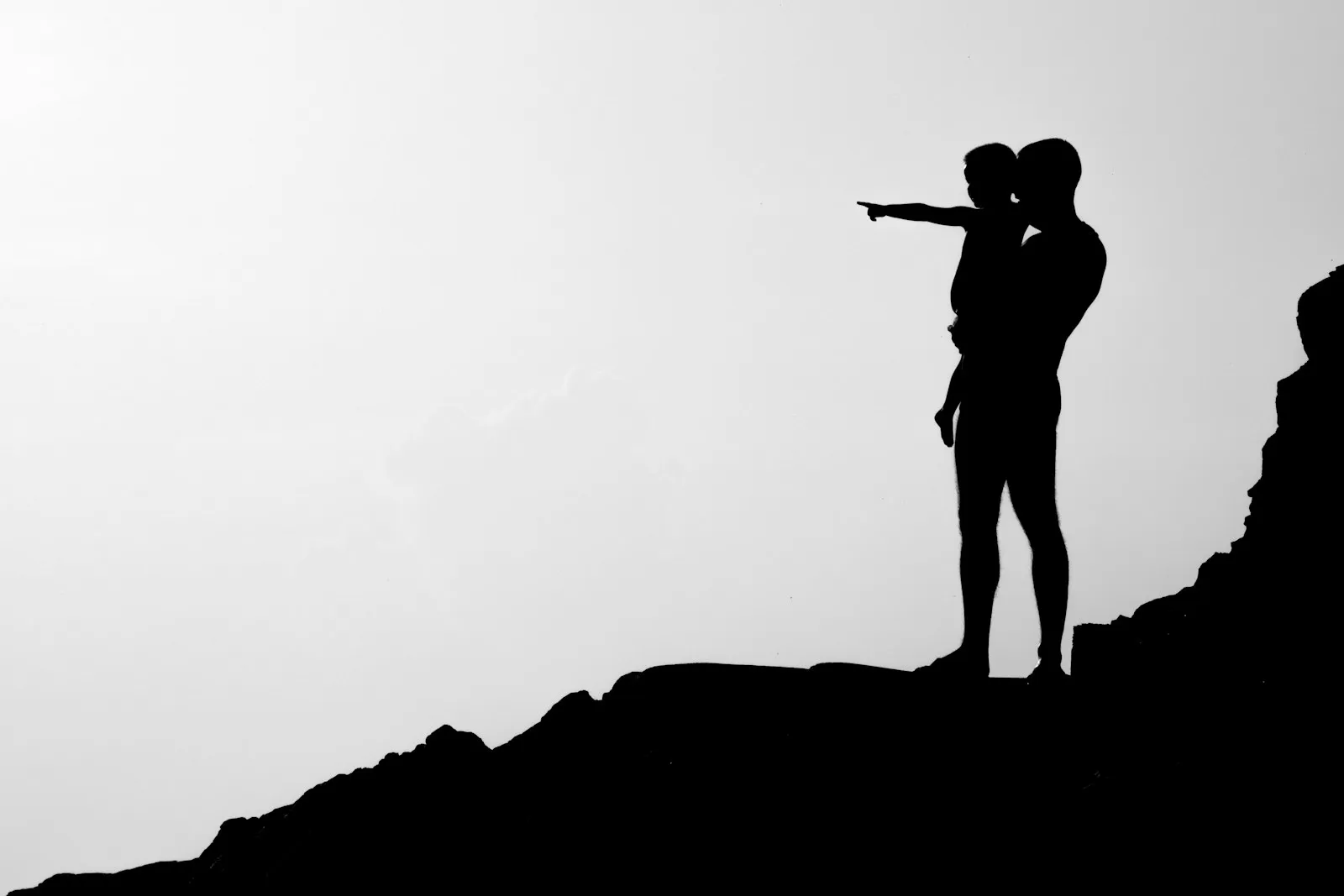 Silhouette of a parent carrying a child against warm light